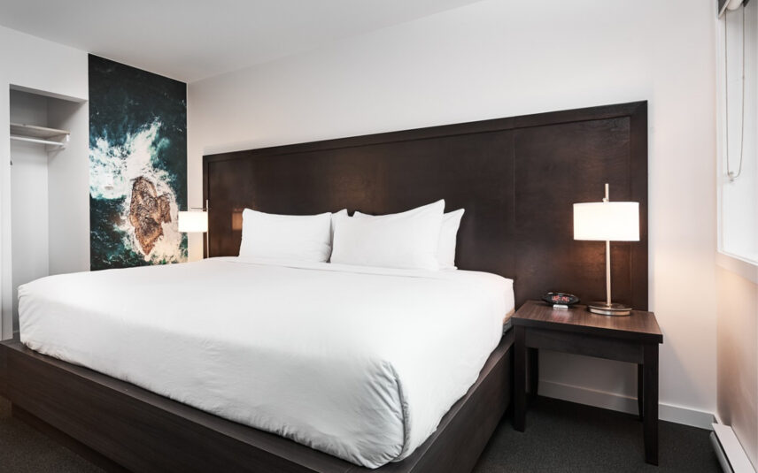 Queen bed with crisp white linens and ocean wave photography above the headboard