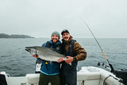 Two smiling anglers proudly hold up a massive fish on deck