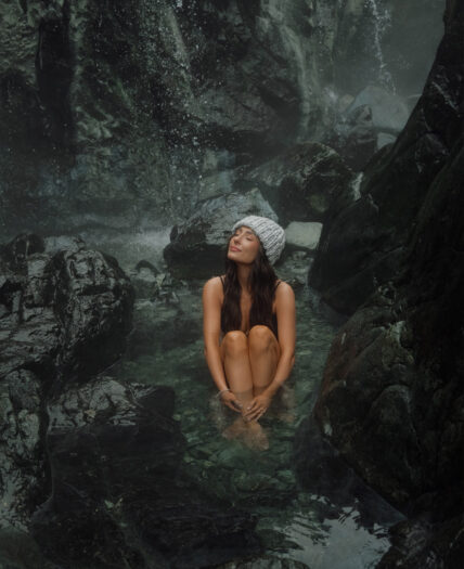 Guest soaking in Tofino’s natural hot springs with a waterfall in the background