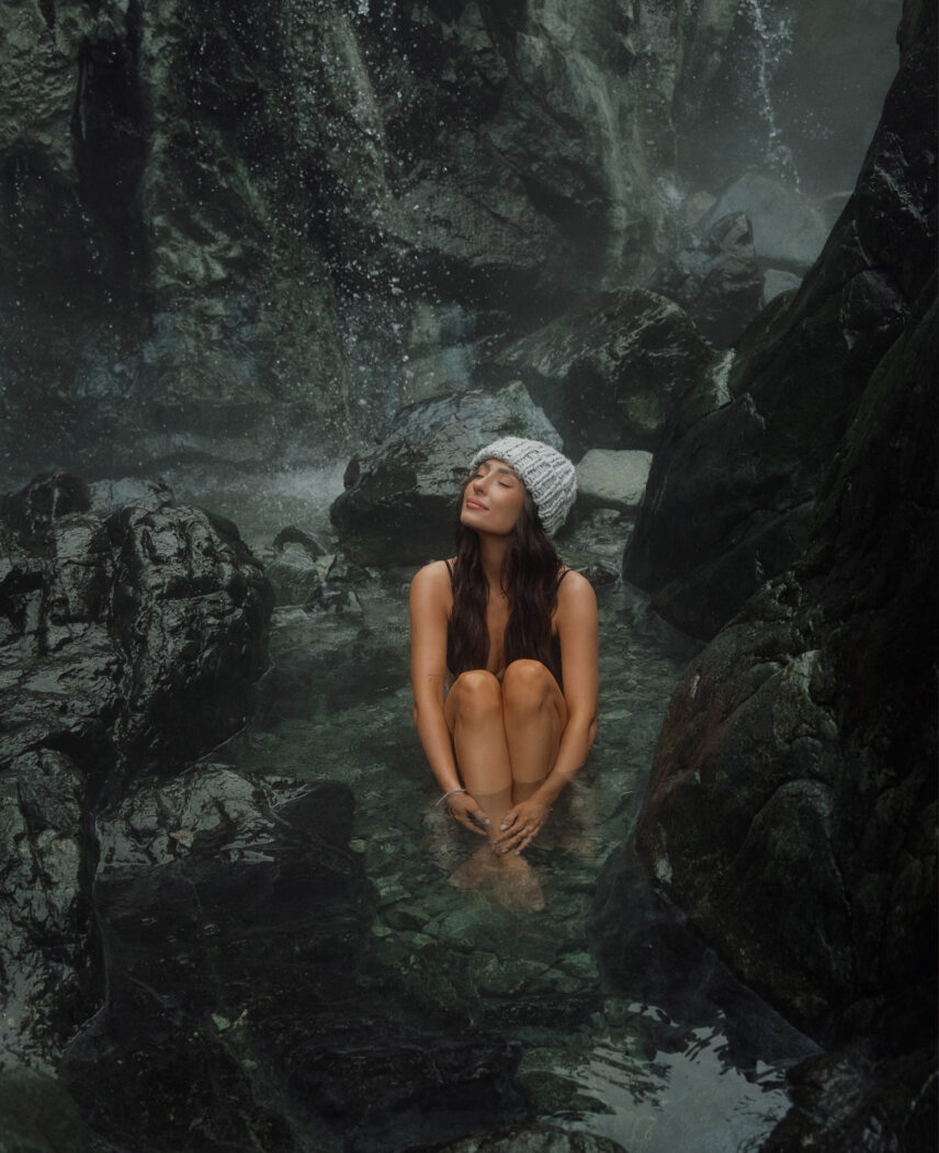 Guest soaking in Tofino’s natural hot springs with a waterfall in the background