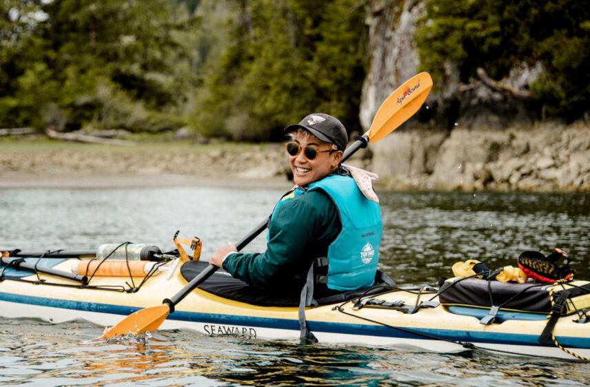 Friendly kayak guide smiling while paddling through a calm West Coast inlet