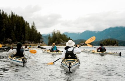 Kayakers paddling through calm waters with scenic views of Tofino’s lush coastline