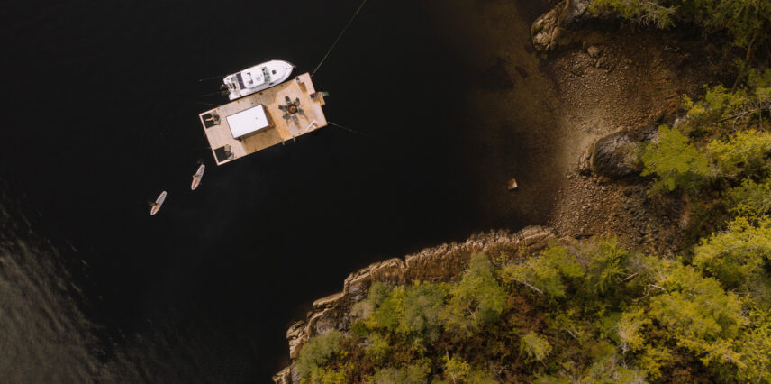 Aerial view of Tofino’s floating sauna docked in Clayoquot Sound with foggy mountains in the background