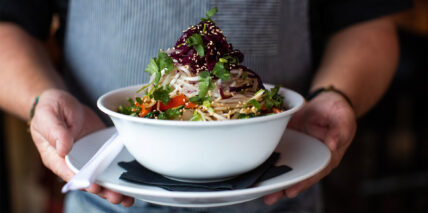 A person holding up a bowl of food in a warmly lit restaurant