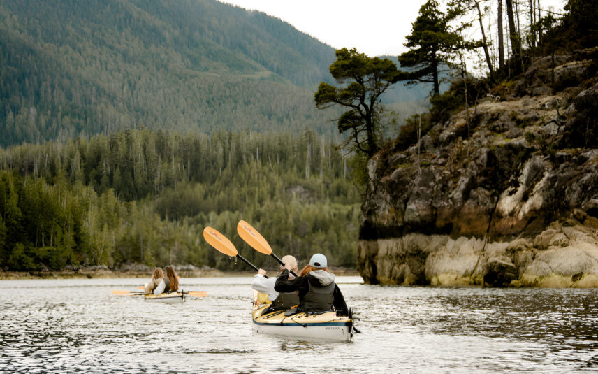 Couple paddling a double sea kayak through the calm waters of a remote Tofino inlet