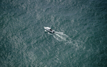 Drone shot of a boat cruising through calm waters near Tofino, surrounded by coastal forest