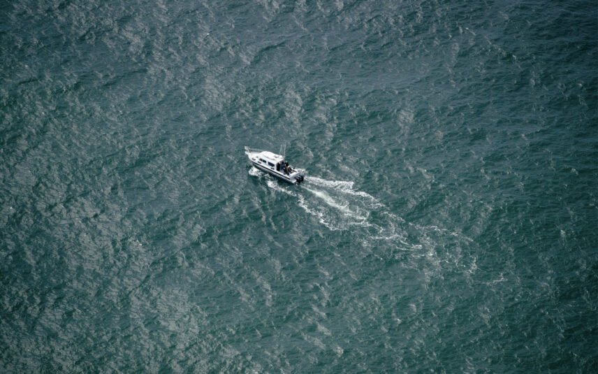 Drone shot of a boat cruising through calm waters near Tofino, surrounded by coastal forest