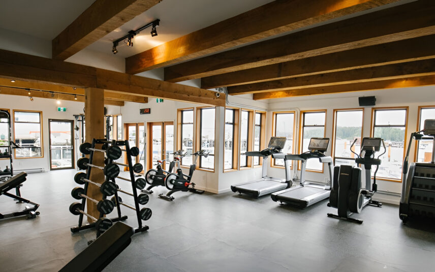 Light-filled gym at Tofino Resort + Marina with cardio and weight equipment overlooking the harbour