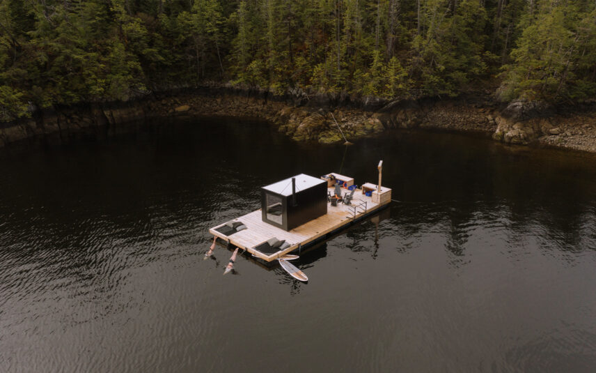 Aerial view of Tofino’s remote floating sauna with guests diving into the ocean from the dock