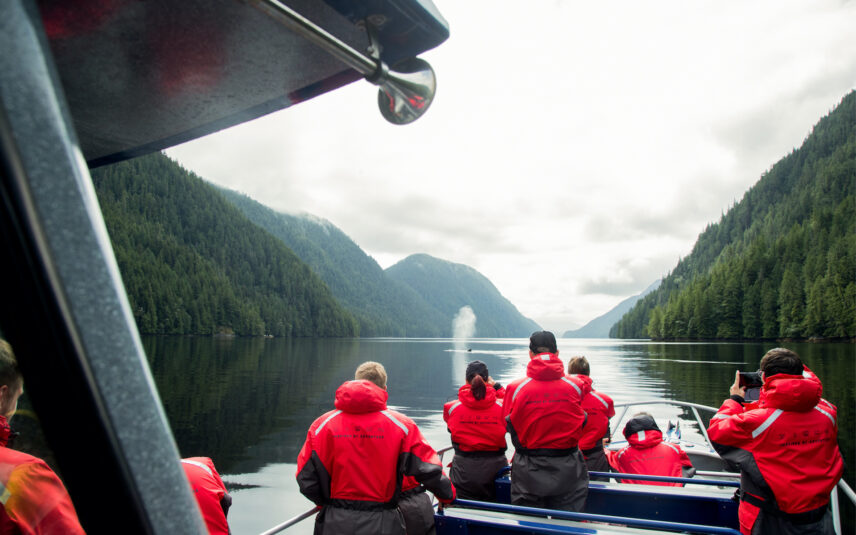 Team in red jackets on a boat watching a whale spout in the Pacific Ocean off Tofino