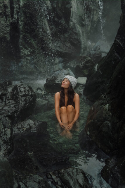 Woman relaxing in a geothermal rock pool at Hot Springs Cove with a natural waterfall in the background