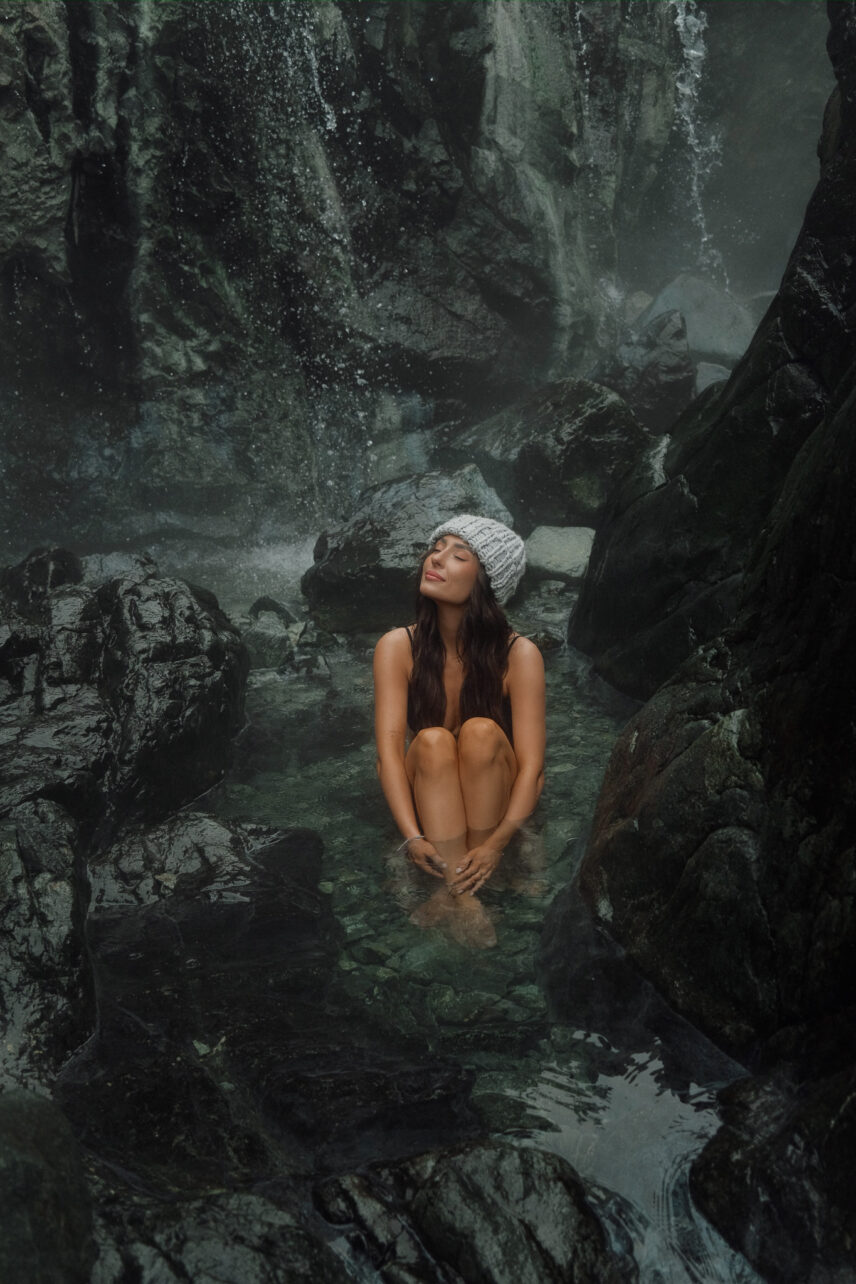 Woman relaxing in a geothermal rock pool at Hot Springs Cove with a natural waterfall in the background