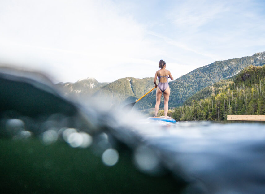 Half underwater shot of woman paddle boarding near the floating sauna in Tofino