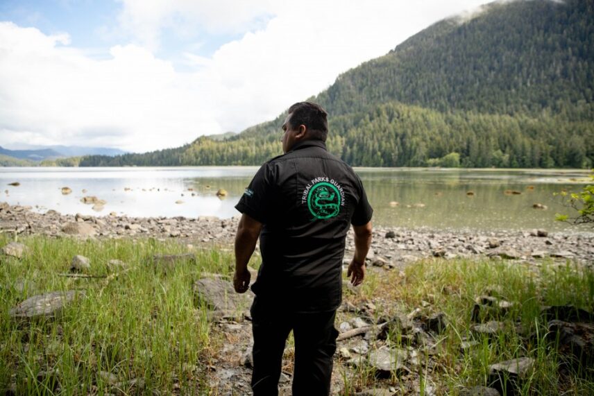 Man overlooking the ocean and forest wearing a Tribal Parks Guardian shirt