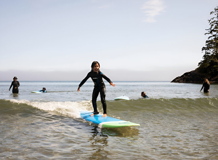 Young child surfing a small wave, smiling with arms outstretched