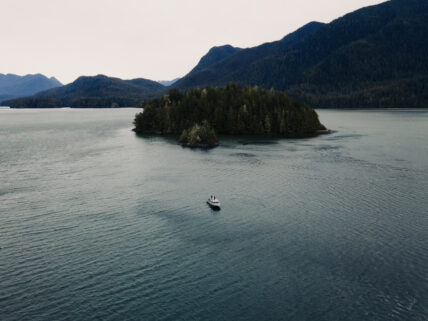 Aerial view of a boat cruising through the vivid green waters of Clayoquot Sound