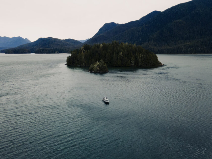 Aerial view of a boat cruising through the vivid green waters of Clayoquot Sound