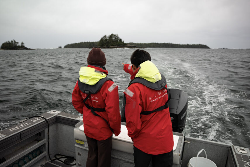 Two guests in red jackets pointing toward the horizon while standing on a boat