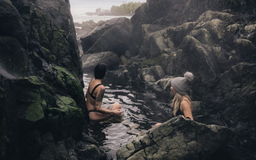 Two women soaking in Hot Springs Cove, looking out to the misty Pacific Ocean