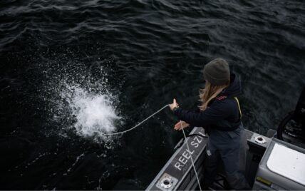 Captain throwing a crab trap into the ocean from the Reel Season boat, water splashing on impact