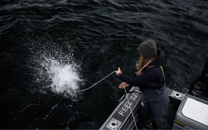 Captain throwing a crab trap into the ocean from the Reel Season boat, water splashing on impact