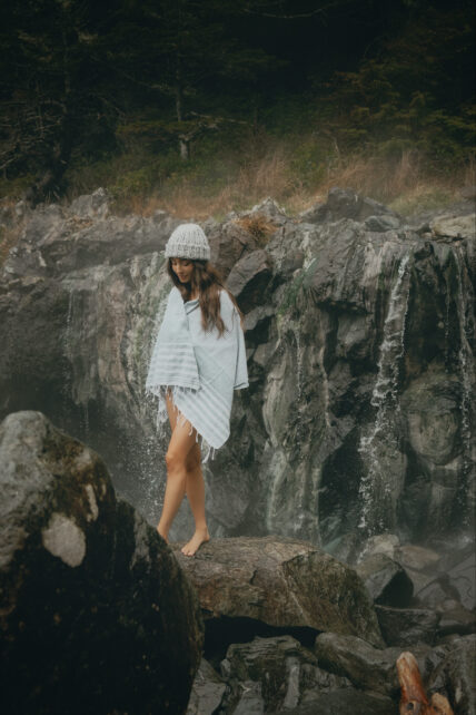 Woman walking across coastal rocks wrapped in a towel near Hot Springs Cove