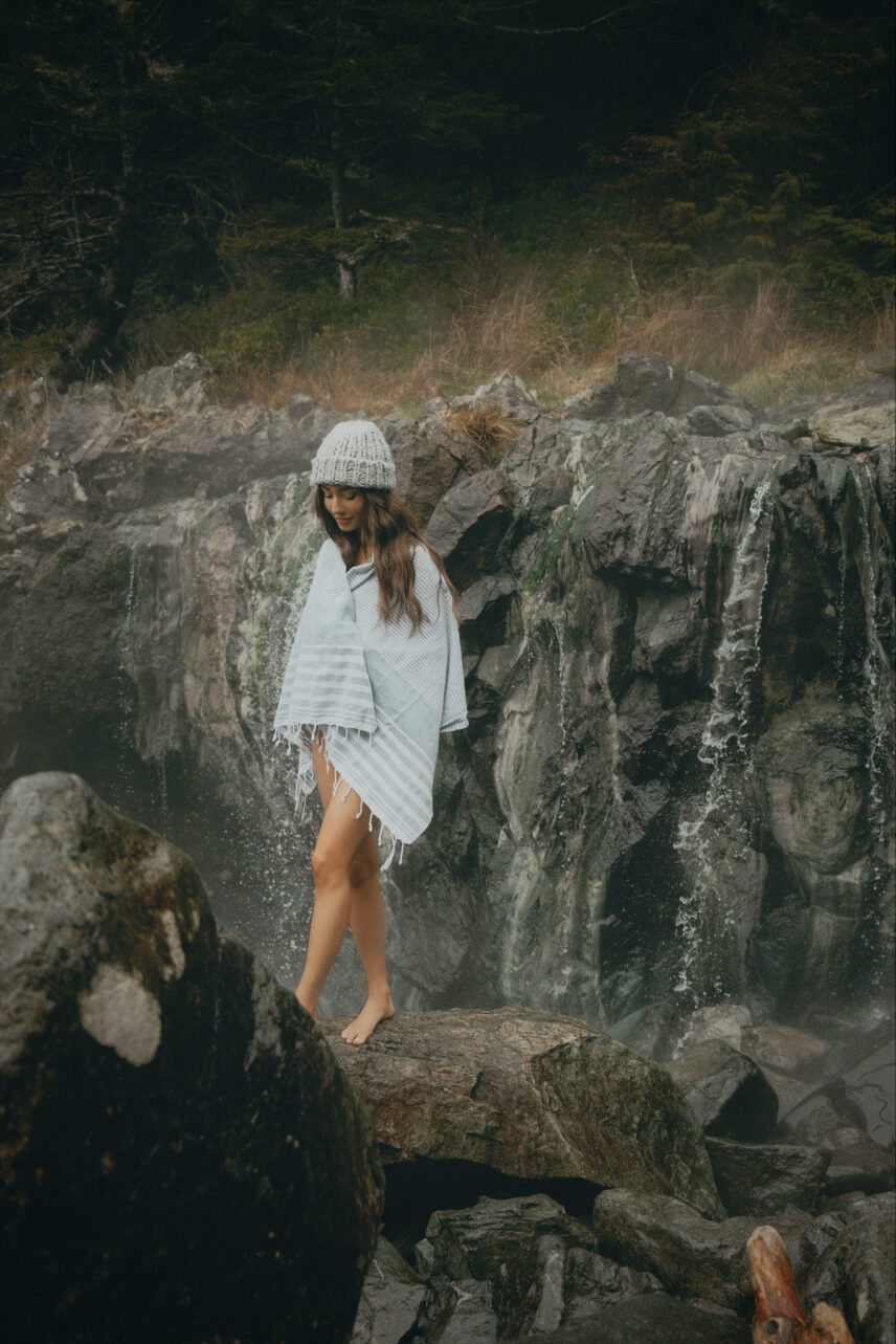 Woman walking across coastal rocks wrapped in a towel near Hot Springs Cove