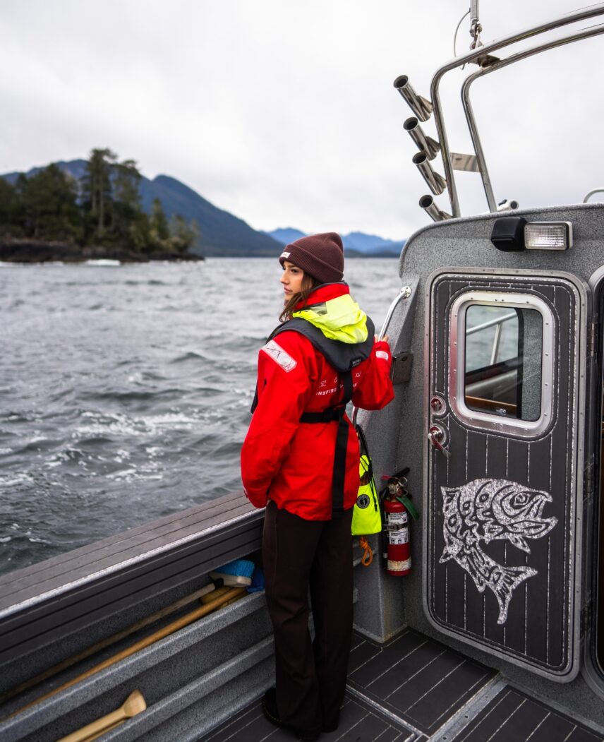 Woman in Tofino Resort + Marina’s signature red jacket standing near the boat Blackfish with inlet views